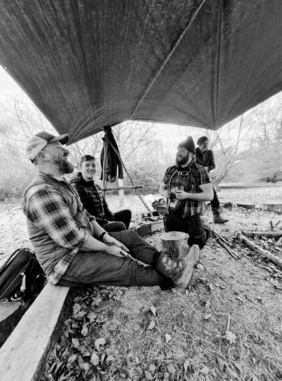 A group sitting together beneath a woodland shelter